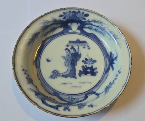 fig 1. A circular Edo period Japanese Arita porcelain shallow dish featuring hand-painted cobalt blue underglaze figurative and floral decoration on an off-white ceramic body.