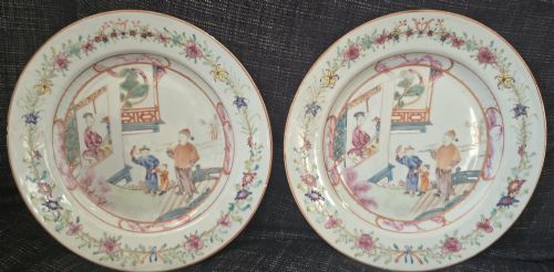 fig 1. A pair of circular white porcelain plates hand-painted with famille rose enamels depicting figures in an interior and garden setting with a floral rim border.