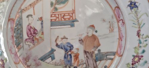 fig 4. A pair of circular white porcelain plates hand-painted with famille rose enamels depicting figures in an interior and garden setting with a floral rim border.