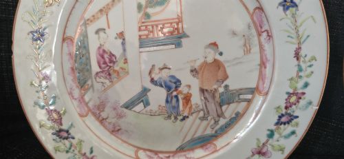 fig 5. A pair of circular white porcelain plates hand-painted with famille rose enamels depicting figures in an interior and garden setting with a floral rim border.