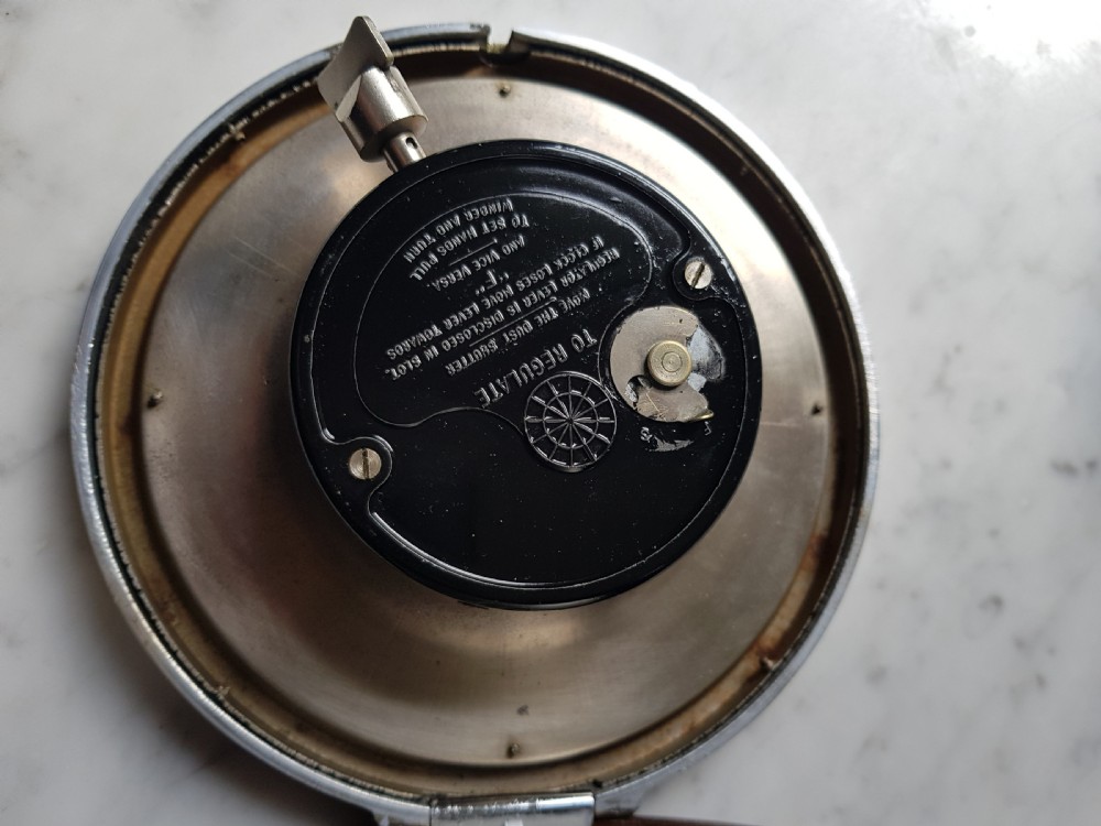 A circular vintage Smiths London Passenger Transport Board clock featuring a black dial, white Arabic numerals, luminous hands, and a chrome bezel. View V