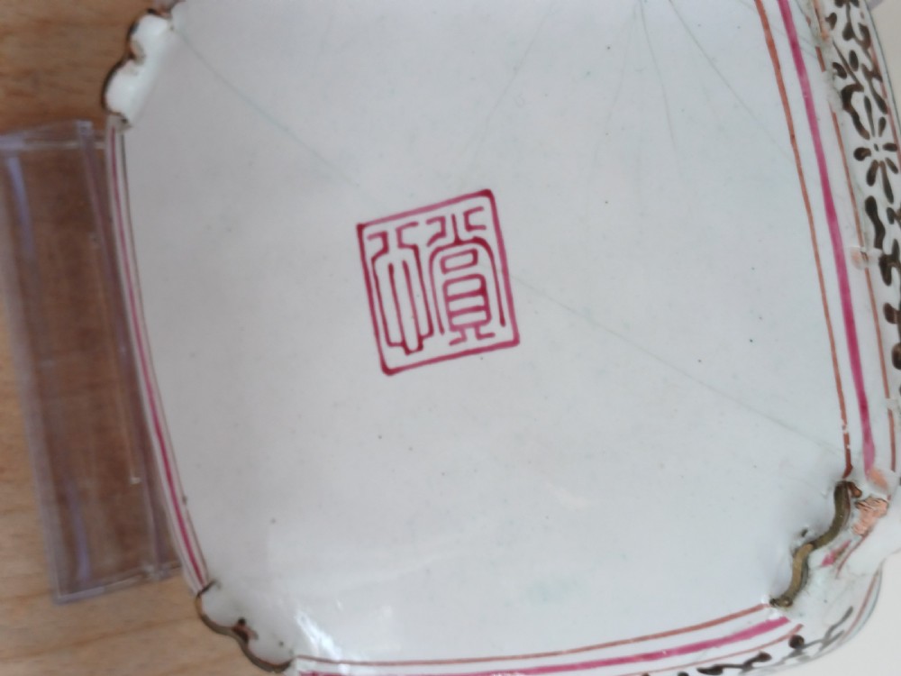 A square 18th-century Chinese Canton enamel dish with lobed corners, depicting figures in a landscape in famille rose enamels framed by a patterned border. View IX