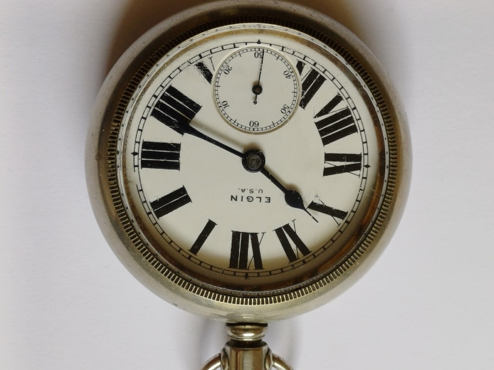 An open-face antique pocket watch featuring a white enamel dial with black Roman numerals, a sub-seconds dial, and a silver-tone nickel case. View II