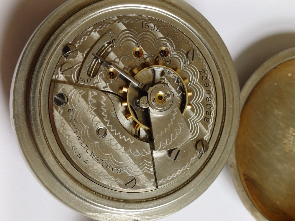 An open-face antique pocket watch featuring a white enamel dial with black Roman numerals, a sub-seconds dial, and a silver-tone nickel case. View XI