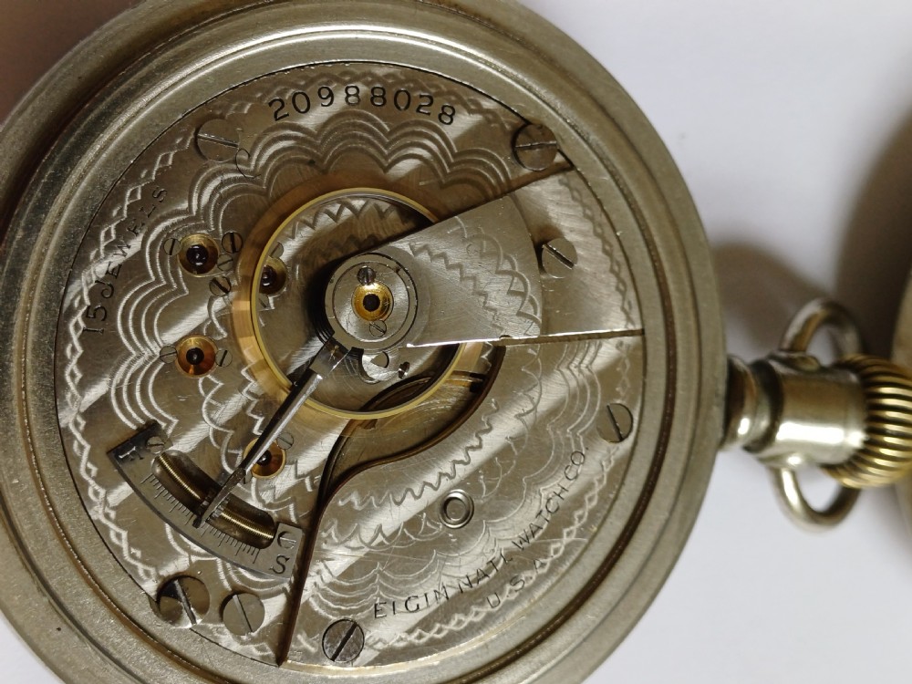 An open-face antique pocket watch featuring a white enamel dial with black Roman numerals, a sub-seconds dial, and a silver-tone nickel case. View XIII