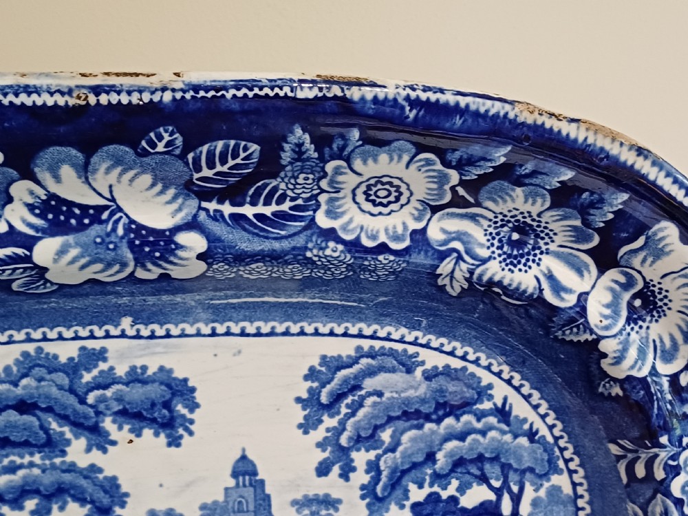 A large Victorian oval earthenware platter decorated with a cobalt blue and white transfer print featuring a pastoral river scene and a wide floral border. View III