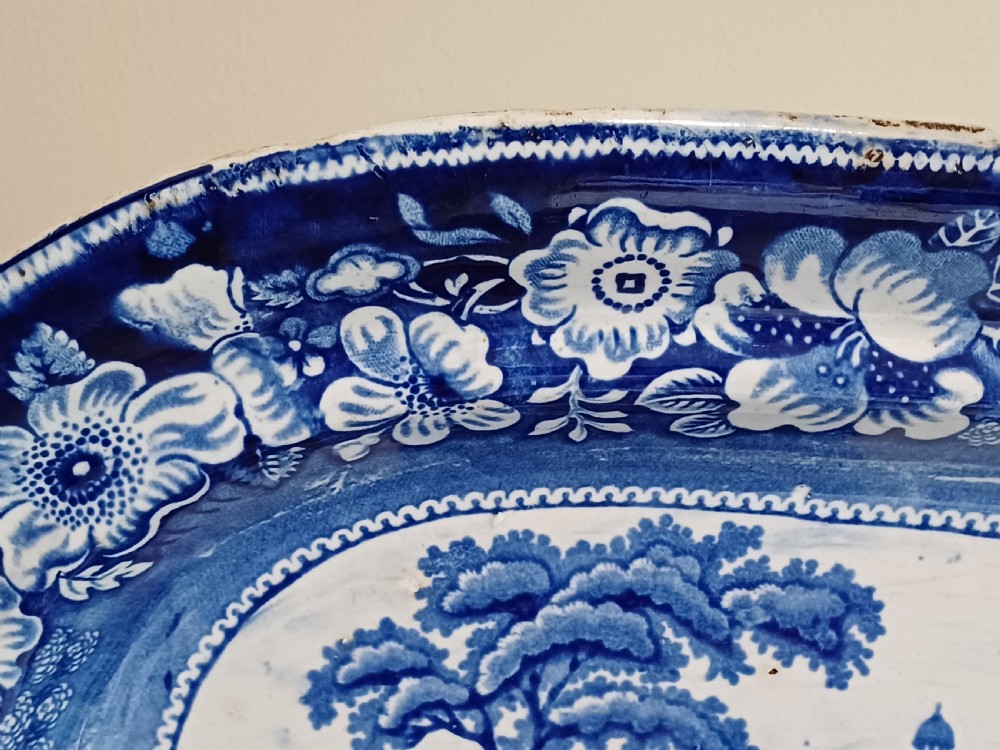 A large Victorian oval earthenware platter decorated with a cobalt blue and white transfer print featuring a pastoral river scene and a wide floral border. View IV