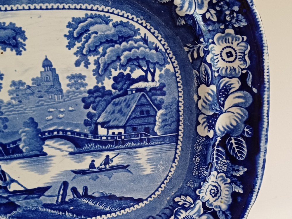 A large Victorian oval earthenware platter decorated with a cobalt blue and white transfer print featuring a pastoral river scene and a wide floral border. View VIII