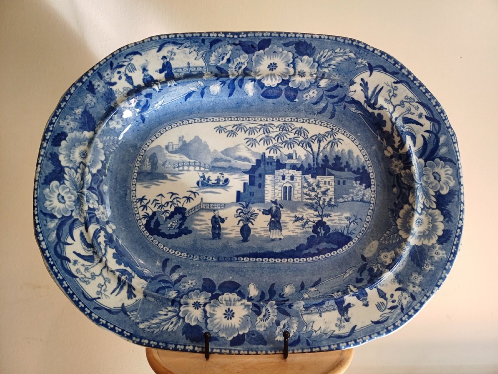 A large oval blue and white earthenware meat platter featuring a transfer-printed Chinese garden scene with figures, bridges, and floral borders.