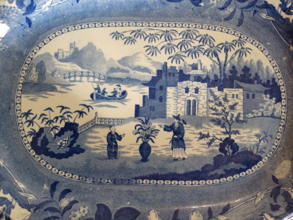 A large oval blue and white earthenware meat platter featuring a transfer-printed Chinese garden scene with figures, bridges, and floral borders. View III