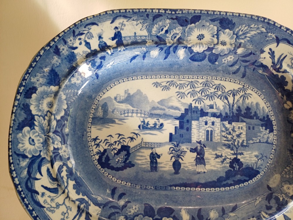 A large oval blue and white earthenware meat platter featuring a transfer-printed Chinese garden scene with figures, bridges, and floral borders. View VI