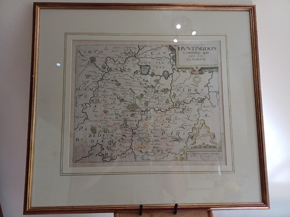 A framed 17th-century hand-coloured map of Huntingdon by Christopher Saxton set within an off-white mount and slim gilded frame.