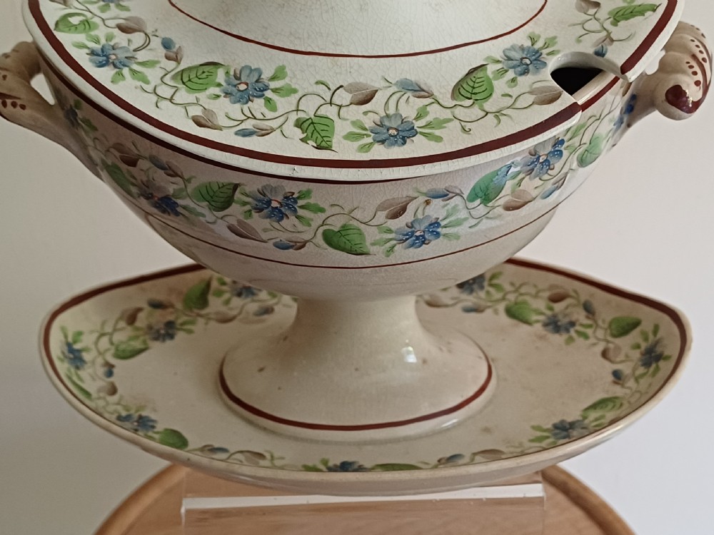 An antique cream earthenware pedestal dessert tureen with matching lid and stand, decorated with a floral vine border in blue and green. View II