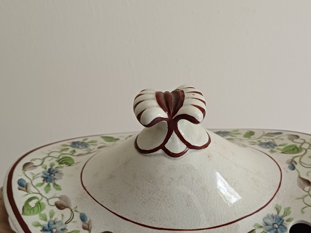 An antique cream earthenware pedestal dessert tureen with matching lid and stand, decorated with a floral vine border in blue and green. View V