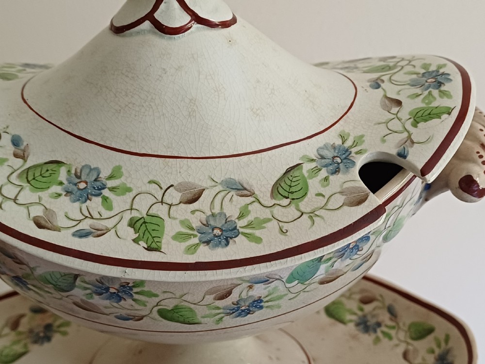An antique cream earthenware pedestal dessert tureen with matching lid and stand, decorated with a floral vine border in blue and green. View VI