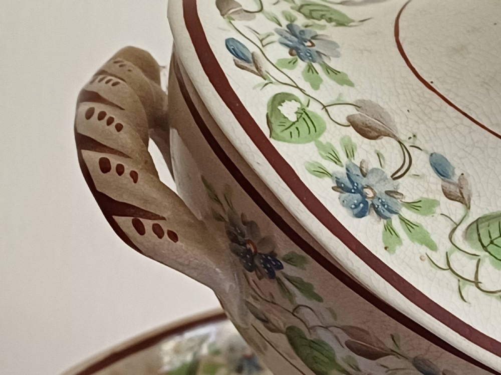 An antique cream earthenware pedestal dessert tureen with matching lid and stand, decorated with a floral vine border in blue and green. View IX