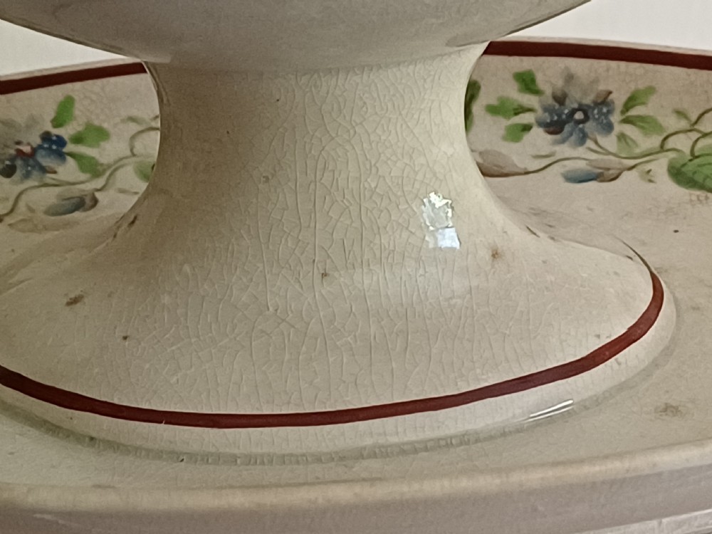 An antique cream earthenware pedestal dessert tureen with matching lid and stand, decorated with a floral vine border in blue and green. View XIV