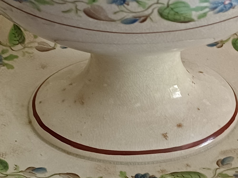 An antique cream earthenware pedestal dessert tureen with matching lid and stand, decorated with a floral vine border in blue and green. View XVII