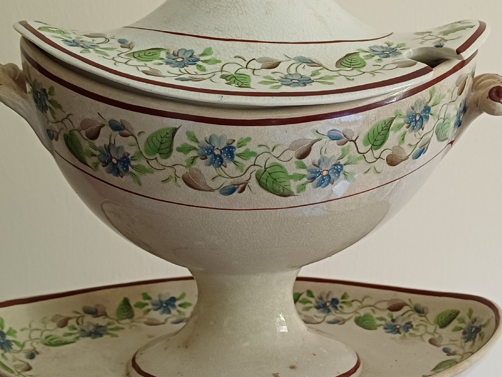 An antique cream earthenware pedestal dessert tureen with matching lid and stand, decorated with a floral vine border in blue and green. View XXI