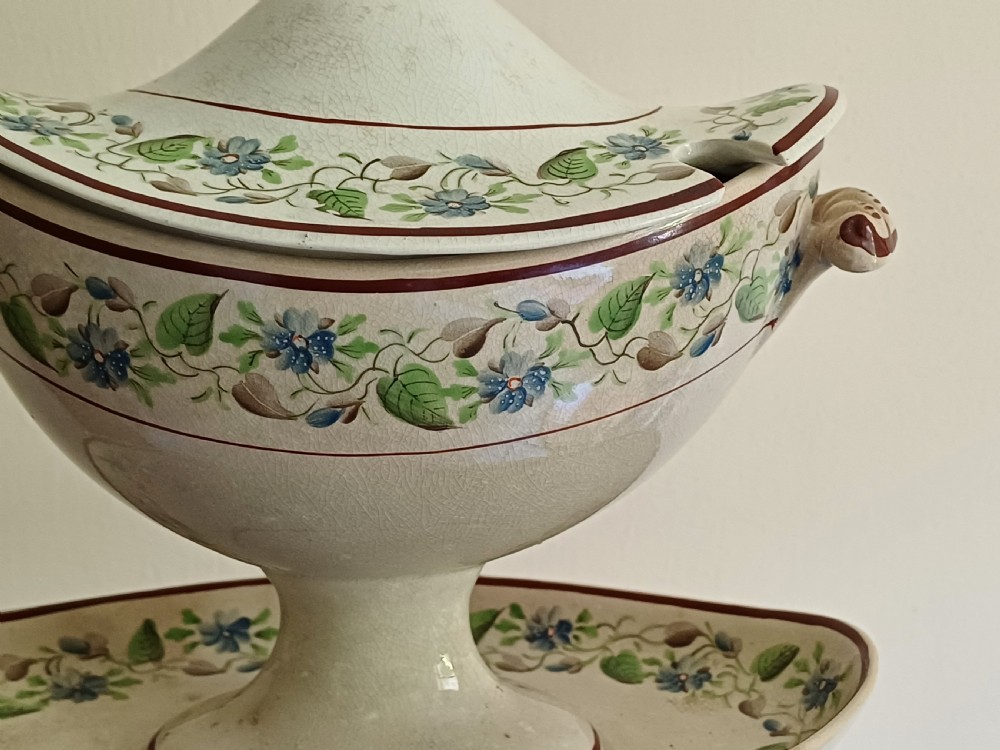 An antique cream earthenware pedestal dessert tureen with matching lid and stand, decorated with a floral vine border in blue and green. View XXII