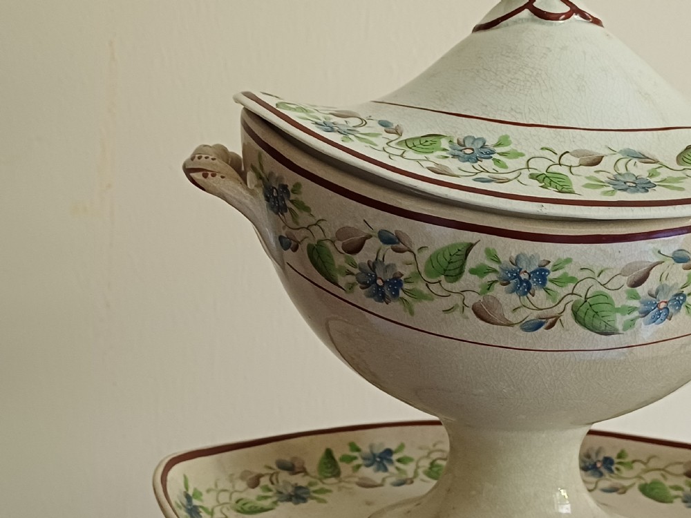 An antique cream earthenware pedestal dessert tureen with matching lid and stand, decorated with a floral vine border in blue and green. View XXIII