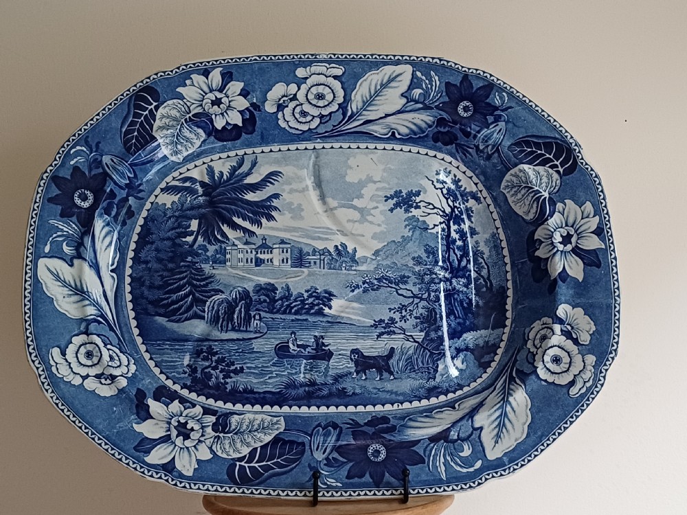 A large oval blue and white transfer printed earthenware meat platter featuring a country landscape scene with a dog and a moulded gravy well channel.