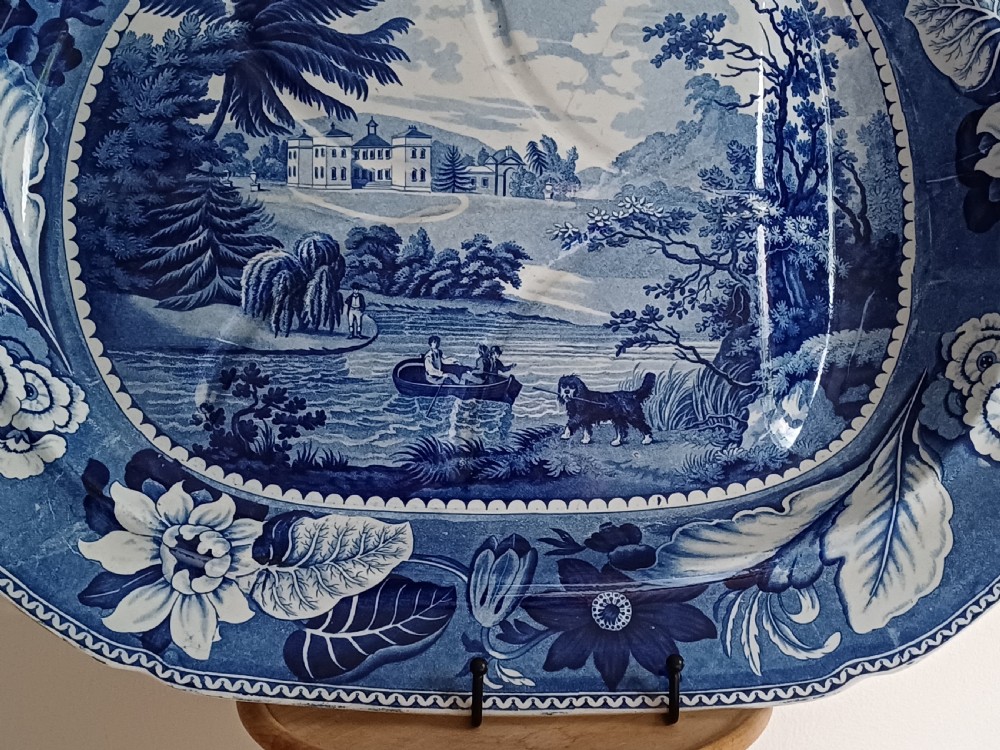 A large oval blue and white transfer printed earthenware meat platter featuring a country landscape scene with a dog and a moulded gravy well channel. View III
