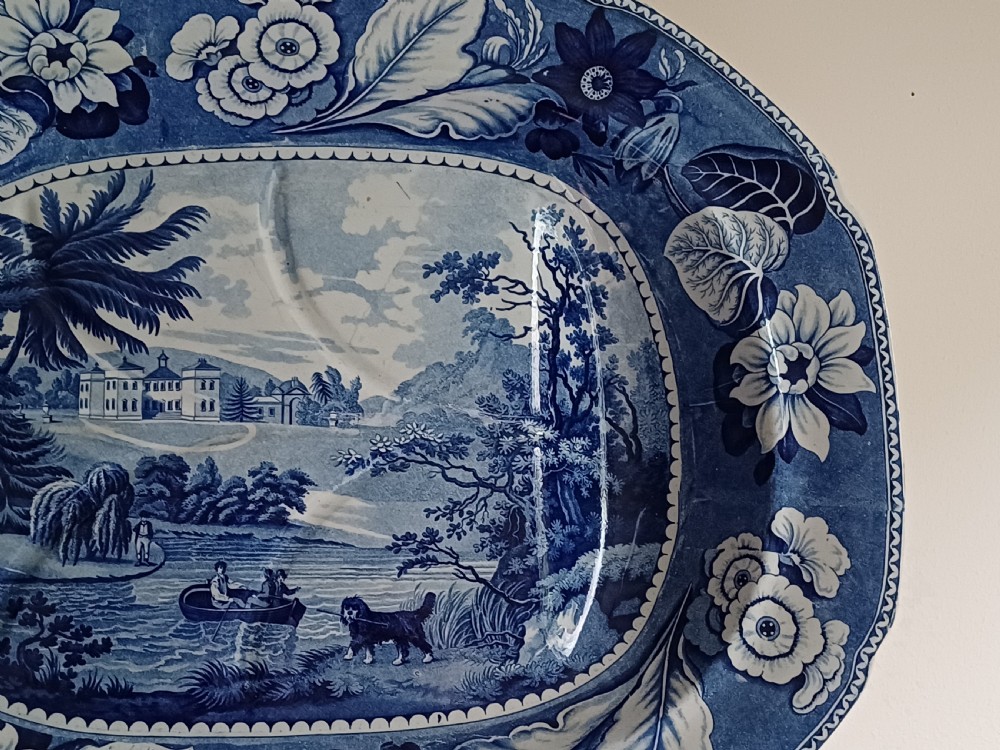 A large oval blue and white transfer printed earthenware meat platter featuring a country landscape scene with a dog and a moulded gravy well channel. View IV