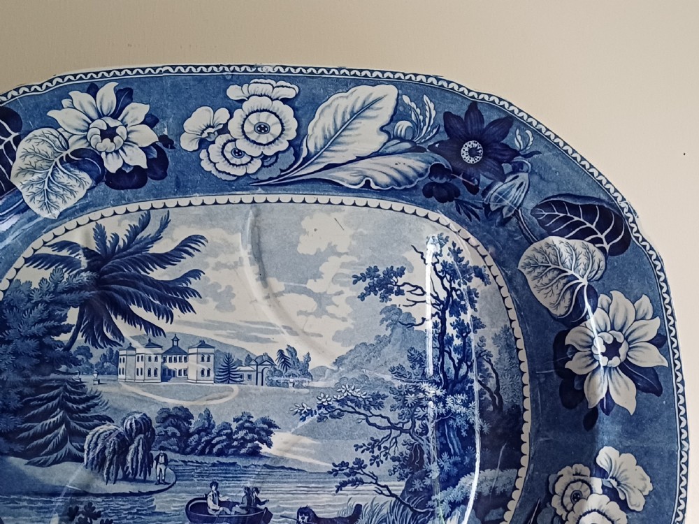 A large oval blue and white transfer printed earthenware meat platter featuring a country landscape scene with a dog and a moulded gravy well channel. View V