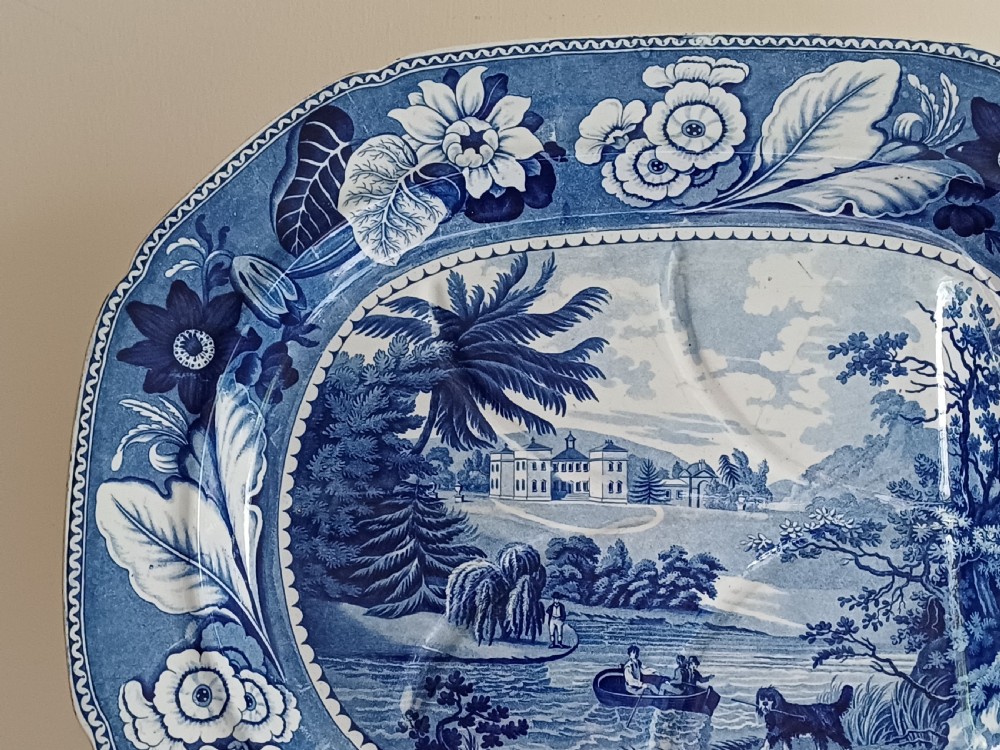 A large oval blue and white transfer printed earthenware meat platter featuring a country landscape scene with a dog and a moulded gravy well channel. View VI