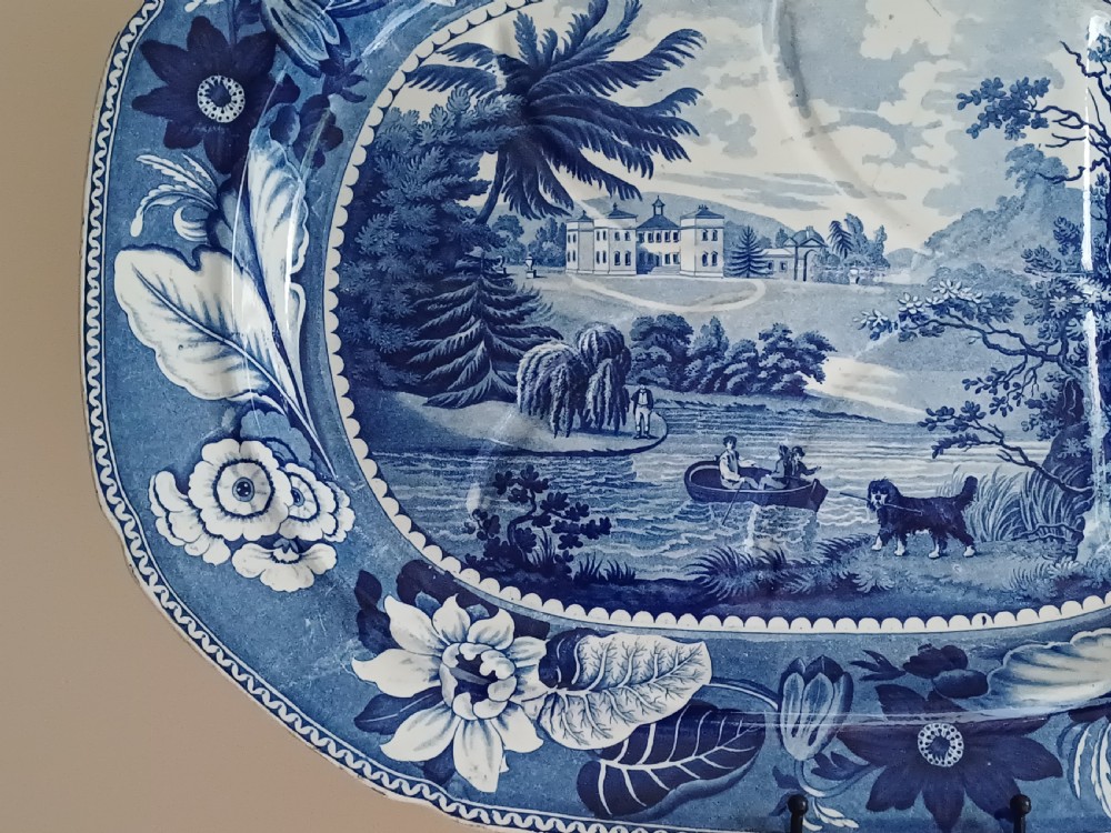 A large oval blue and white transfer printed earthenware meat platter featuring a country landscape scene with a dog and a moulded gravy well channel. View VII
