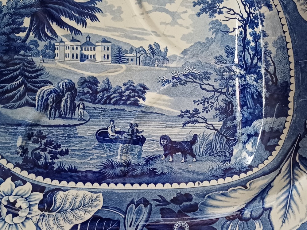 A large oval blue and white transfer printed earthenware meat platter featuring a country landscape scene with a dog and a moulded gravy well channel. View VIII