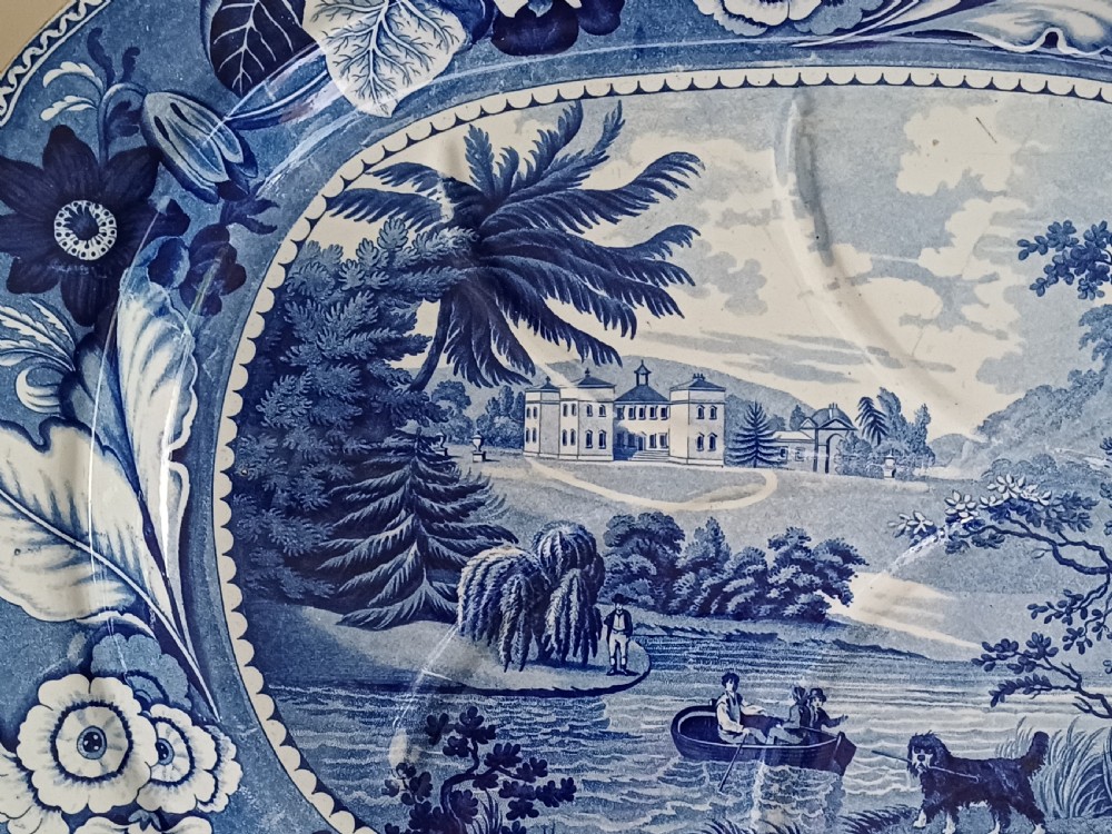 A large oval blue and white transfer printed earthenware meat platter featuring a country landscape scene with a dog and a moulded gravy well channel. View IX