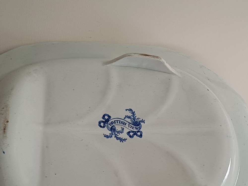 A large oval blue and white transfer printed earthenware meat platter featuring a country landscape scene with a dog and a moulded gravy well channel. View XIV