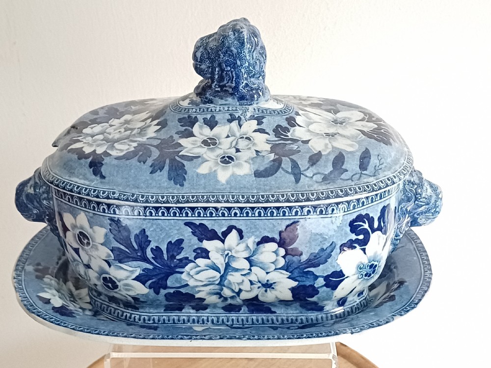 A Georgian blue and white transfer-printed ceramic sauce tureen featuring floral patterns, lion head side handles, a lion finial lid, and a matching underplate.
