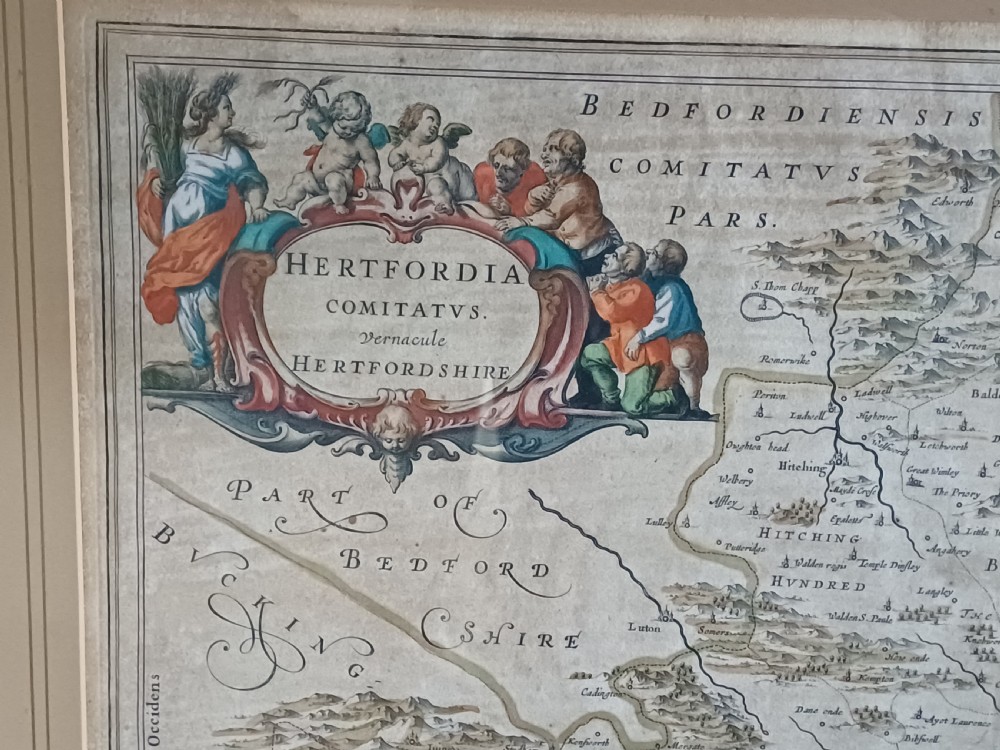 A framed 17th-century hand-coloured map of Hertfordshire by cartographer Jan Blaeu featuring decorative heraldic coats of arms and a title cartouche. View IV