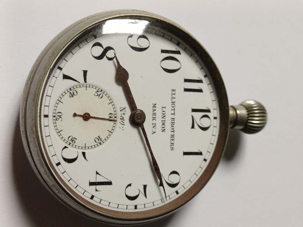 An antique First World War era military pocket watch with a white enamel dial, black Arabic numerals, and a nickel-plated metal case.
