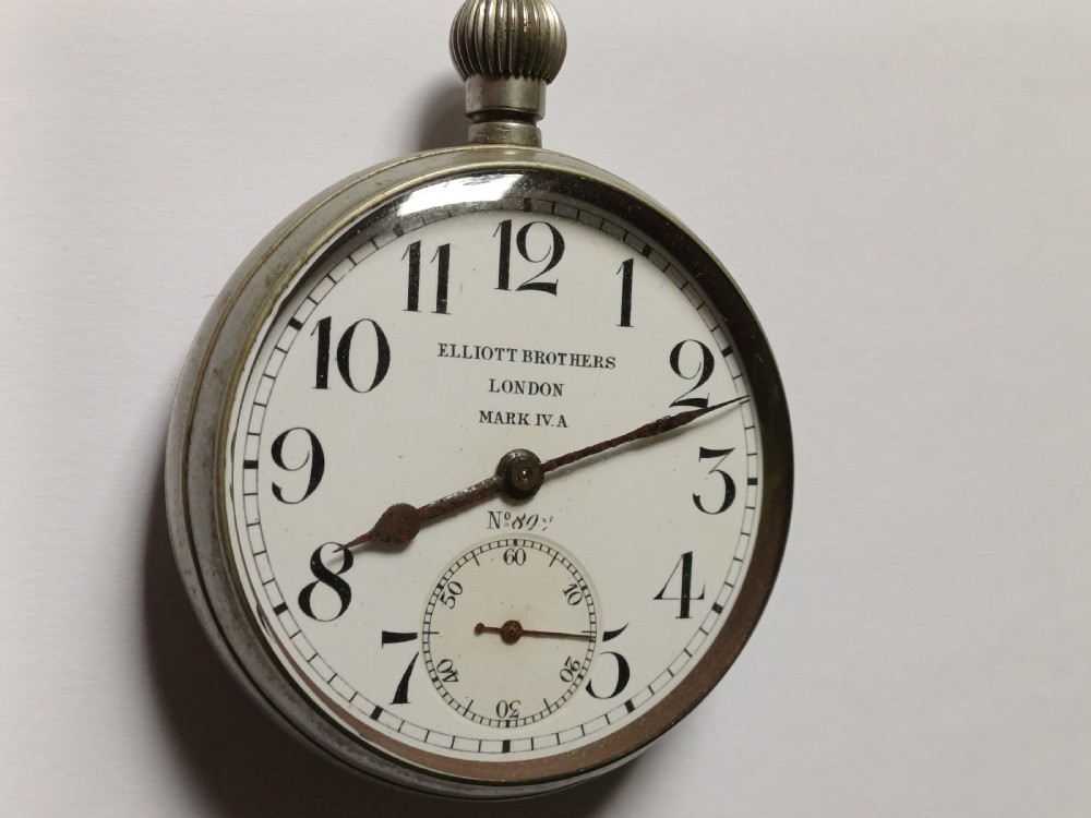 An antique First World War era military pocket watch with a white enamel dial, black Arabic numerals, and a nickel-plated metal case. View III
