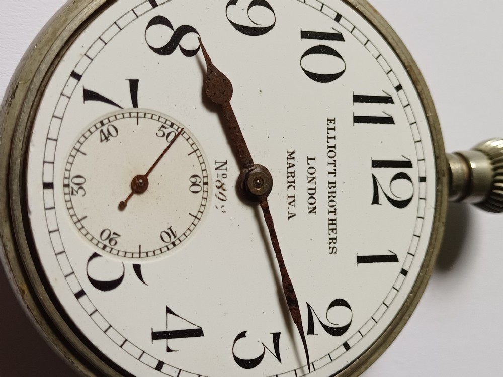 An antique First World War era military pocket watch with a white enamel dial, black Arabic numerals, and a nickel-plated metal case. View V
