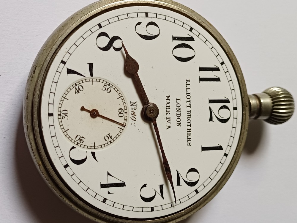 An antique First World War era military pocket watch with a white enamel dial, black Arabic numerals, and a nickel-plated metal case. View VI