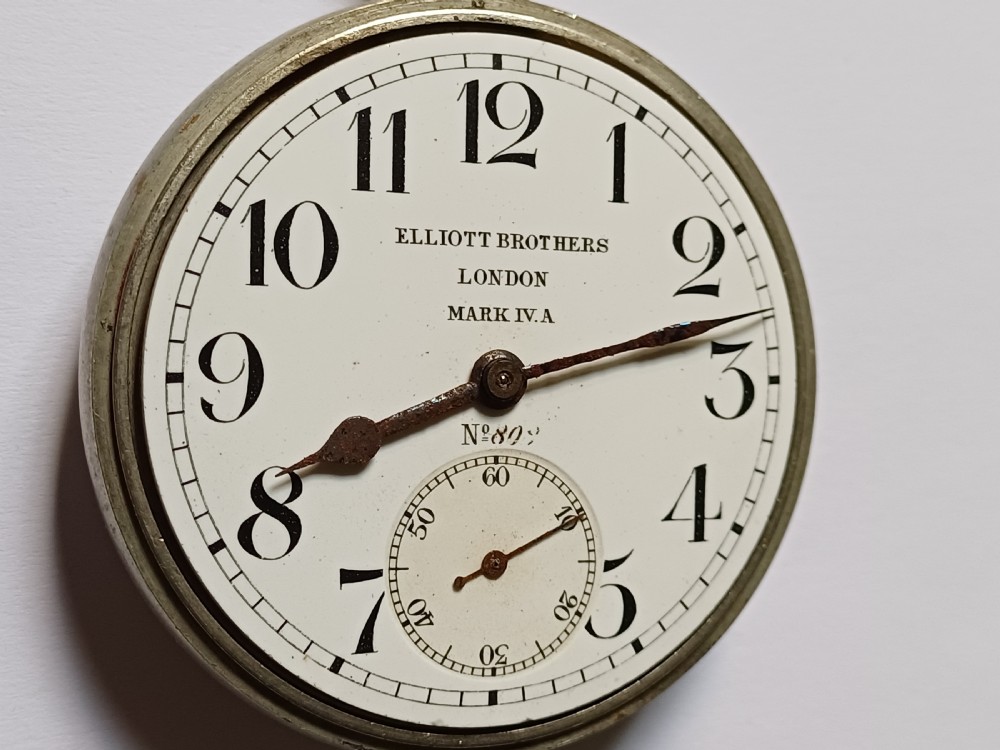 An antique First World War era military pocket watch with a white enamel dial, black Arabic numerals, and a nickel-plated metal case. View VII