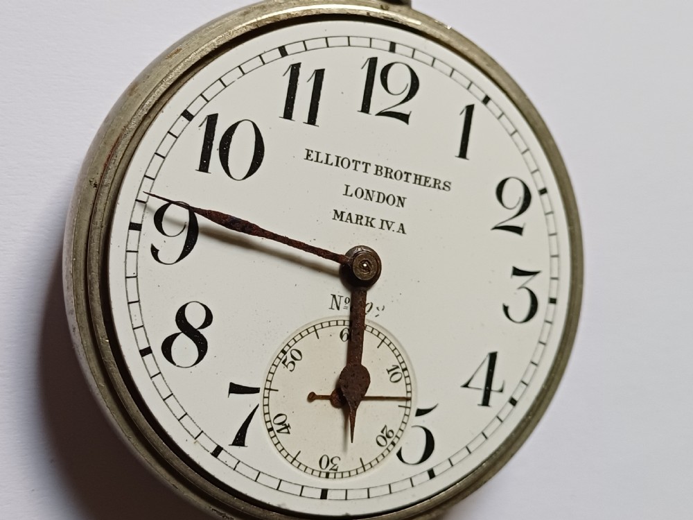 An antique First World War era military pocket watch with a white enamel dial, black Arabic numerals, and a nickel-plated metal case. View IX