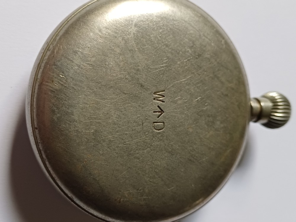 An antique First World War era military pocket watch with a white enamel dial, black Arabic numerals, and a nickel-plated metal case. View X