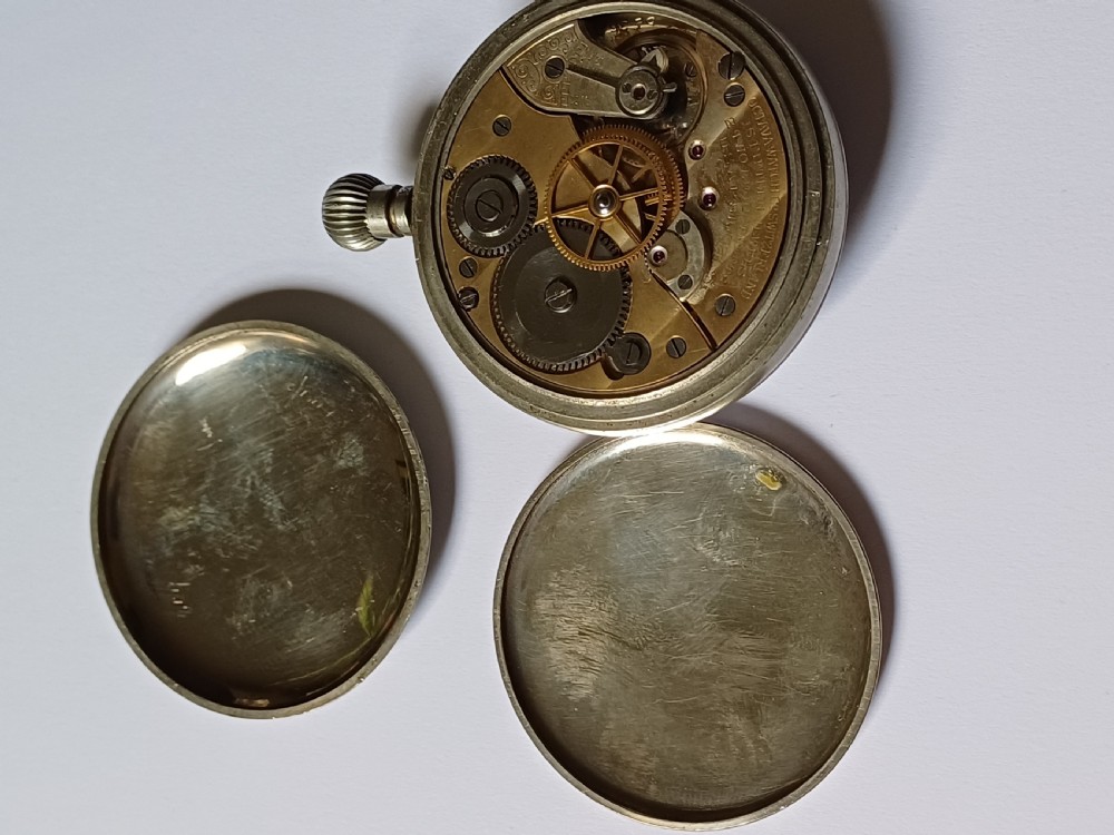 An antique First World War era military pocket watch with a white enamel dial, black Arabic numerals, and a nickel-plated metal case. View XII