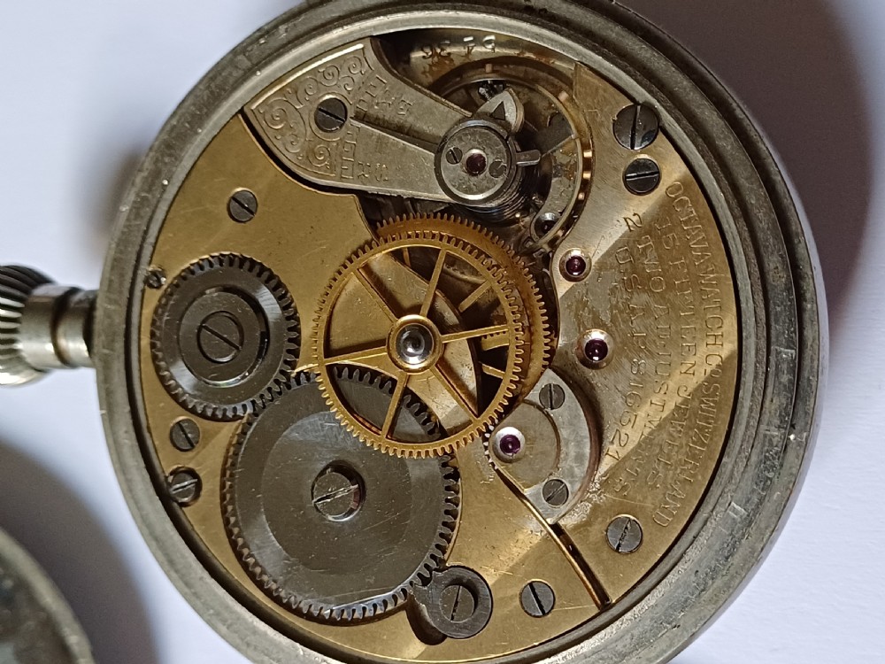 An antique First World War era military pocket watch with a white enamel dial, black Arabic numerals, and a nickel-plated metal case. View XIII