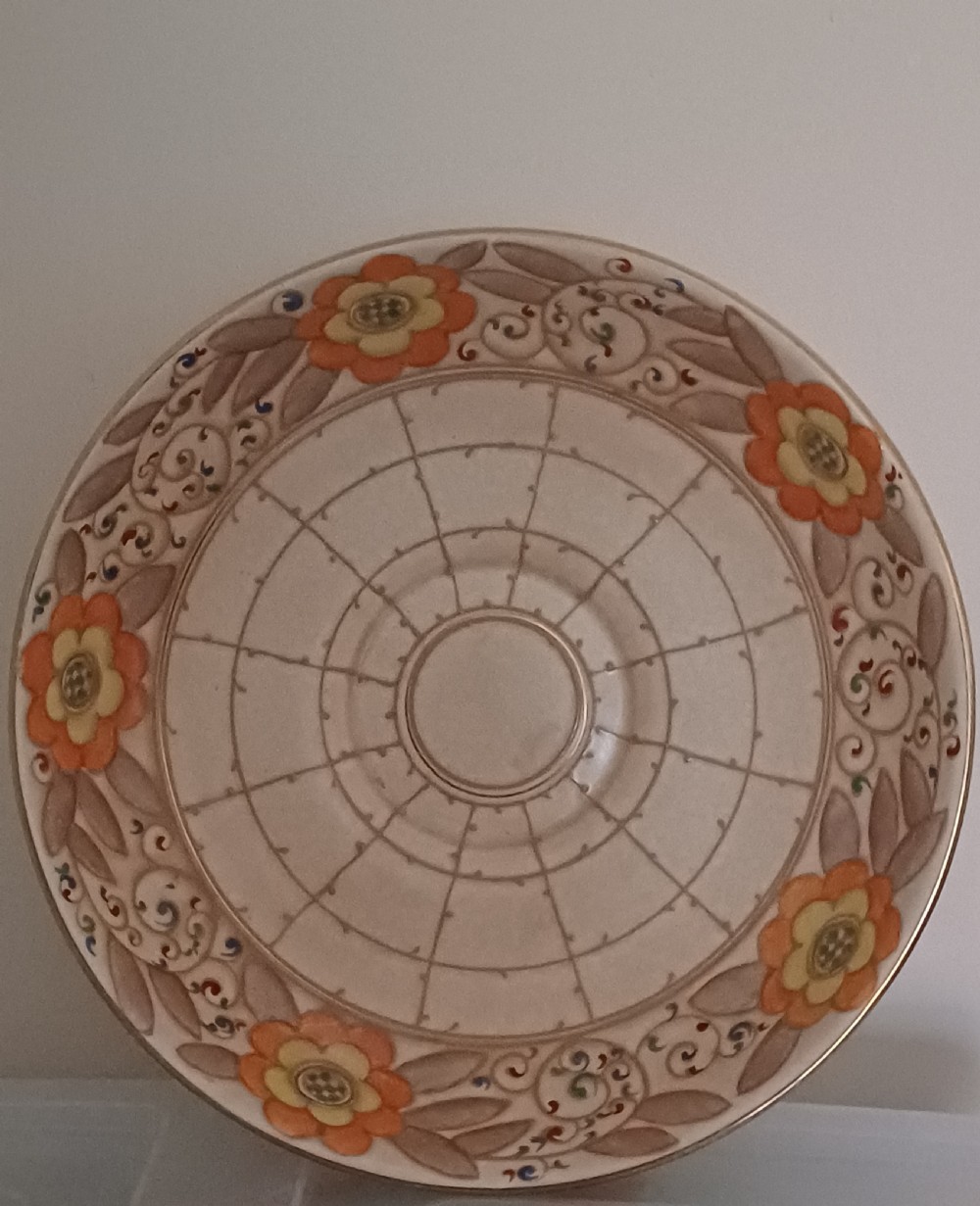 A round Art Deco earthenware bowl featuring a central circular spider-web trellis design surrounded by tube-lined floral motifs in orange and beige.