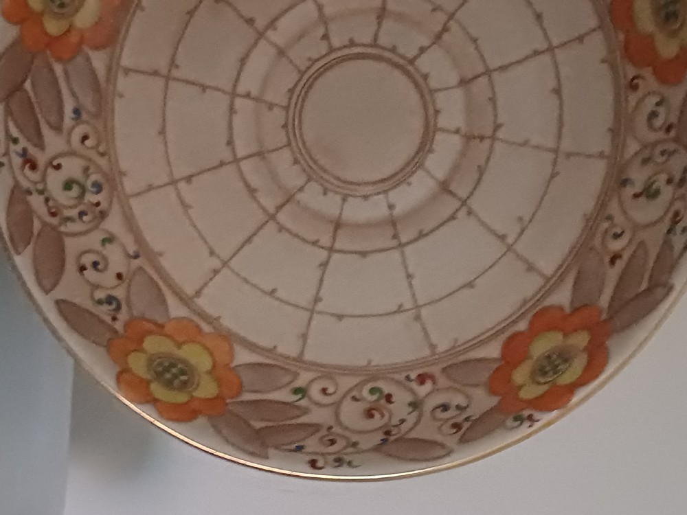 A round Art Deco earthenware bowl featuring a central circular spider-web trellis design surrounded by tube-lined floral motifs in orange and beige. View II