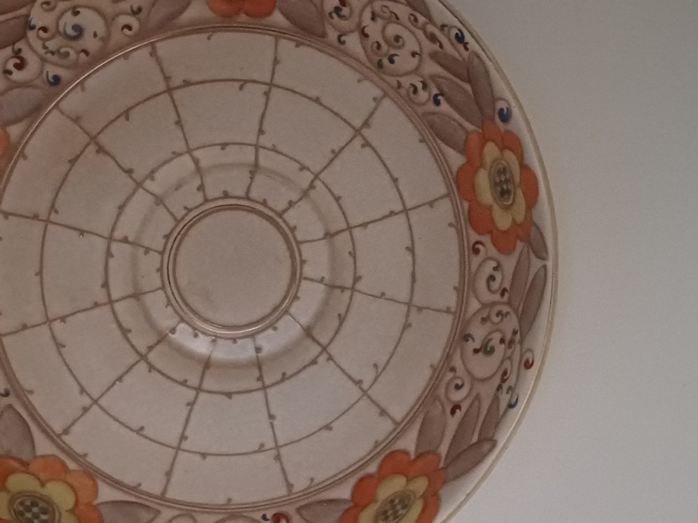 A round Art Deco earthenware bowl featuring a central circular spider-web trellis design surrounded by tube-lined floral motifs in orange and beige. View III