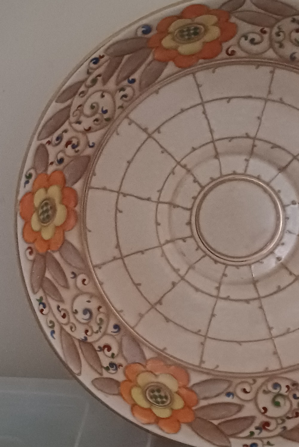 A round Art Deco earthenware bowl featuring a central circular spider-web trellis design surrounded by tube-lined floral motifs in orange and beige. View IV