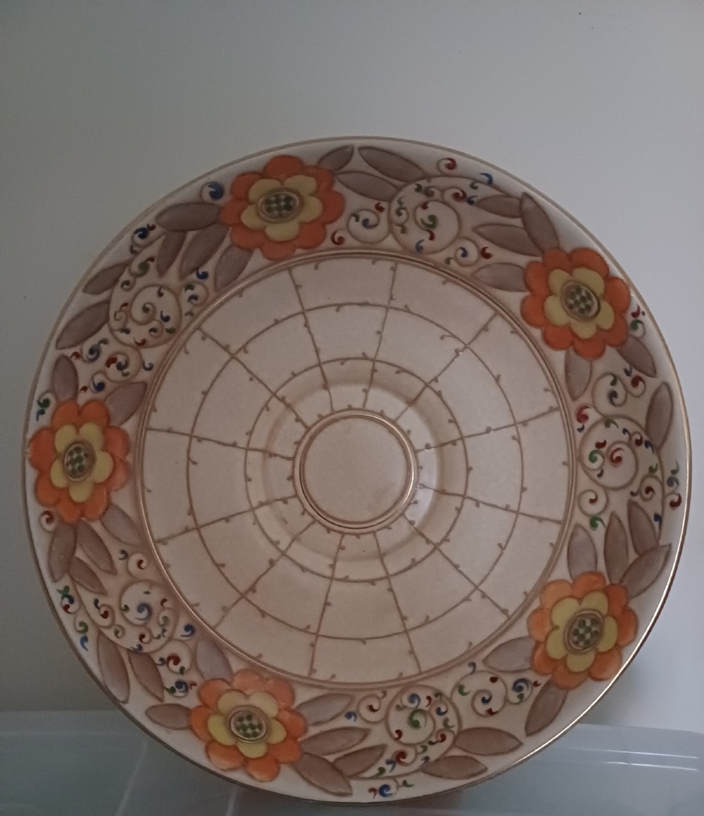 A round Art Deco earthenware bowl featuring a central circular spider-web trellis design surrounded by tube-lined floral motifs in orange and beige. View V